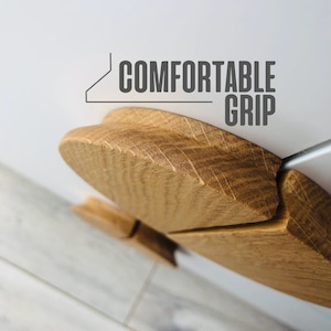 Puede incluir: Primer plano de un tirador de puerta de armario de madera con forma redondeada y curvada. El tirador está hecho de madera marrón claro con un patrón de veta natural. El texto "COMFORTABLE GRIP" es visible sobre el tirador.