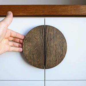 May include: Close-up of a dark brown wooden cabinet door with a circular wooden handle. The handle is split in half and each half is a semi-circle.