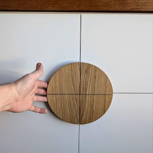 Pode incluir: Um armário branco com um puxador de porta circular de madeira. O puxador é feito de quatro peças de madeira dispostas em círculo. O armário tem um tampo de madeira castanho escuro.