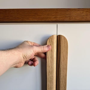 May include: Close-up of a white cabinet door with a wooden handle. The handle is made of two pieces of wood that are joined together in the middle. The handle is curved at the top and bottom.
