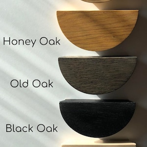 K&ouml;nnte beinhalten: F&uuml;nf halbkreisf&ouml;rmige Holzgriffe f&uuml;r Schubladen, vertikal angeordnet. Die Beschriftungen lauten Clear Oak, Honey Oak, Old Oak, Black Oak und Unfinished. Jeder Griff zeigt eine ausgepr&auml;gte Holzmaserung und ein Finish von hell bis dunkel.