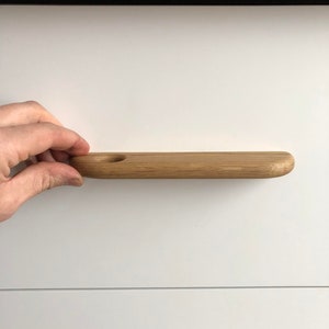 May include: A light brown wooden drawer pull with a round hole in the center. The pull is mounted on a white drawer front.