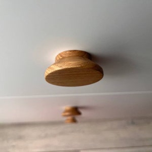 Op de afbeelding: Close-up van een houten kastknop met een afgeronde, licht uitlopende vorm. De knop is gemaakt van lichtbruin hout met een natuurlijke houtnerf.
