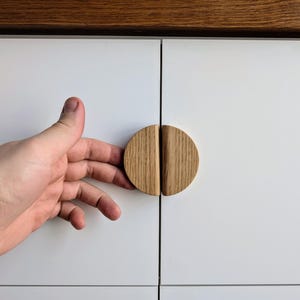 May include: Close-up of a white cabinet door with a wooden, round, split-style cabinet knob. The knob is made of light brown wood and is centered on the door.