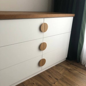 May include: White dresser with four drawers and wooden knobs. The dresser has a light wood top and is sitting on a wood floor.