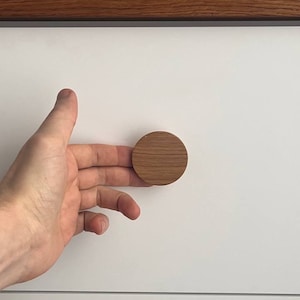 May include: A close-up of a white drawer with a round wooden knob. The knob is made of light brown wood and has a smooth finish.
