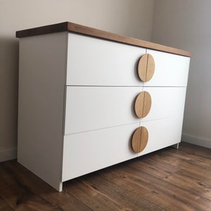 May include: White dresser with three drawers and wooden round knobs. The dresser has a light wood top.