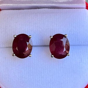 K&ouml;nnte beinhalten: Ein Paar ovale Rubin-Ohrstecker in Silber gefasst. Die tiefroten Edelsteine werden in einer roten Schmuckschatulle mit wei&szlig;em Satin-Innenraum pr&auml;sentiert. Die Ohrringe werden als Schmuckst&uuml;ck pr&auml;sentiert.