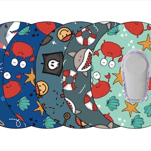 May include: Five colorful round stickers with different sea-themed designs. The stickers feature sharks, crabs, seashells, stars, and a pirate skull. The stickers are designed to be used on medical devices.