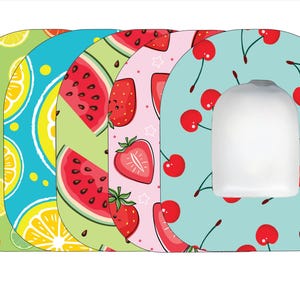 May include: Four different toilet seat covers with various fruit designs. The covers are in a stack, with the top cover featuring a light blue background with red cherries. The second cover has a pink background with red strawberries. The third cover has a green background with red watermelon slices. The bottom cover has a green background with orange slices and lemons.