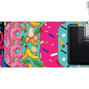 May include: A black medical device with a clear, graduated reservoir and a needle. The device is decorated with colorful patterns including graffiti, pink donuts, bananas, and sprinkles. The background is white.