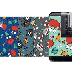 May include: A set of five different patterned fabric squares featuring sharks, crabs, anchors, and pirate skulls. The fabric squares are displayed on a black and clear vape device with a blue and green patterned skin.