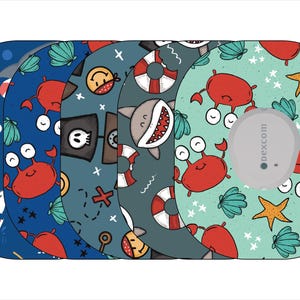 May include: Five different colorful adhesive patches for a continuous glucose monitor (CGM) featuring various sea-themed designs, including sharks, crabs, seashells, and a pirate ship. The patches are designed to be used with a Dexcom CGM.
