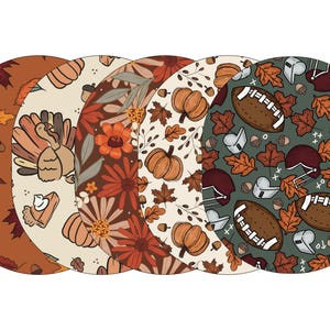 May include: Set of five round placemats featuring different autumn-themed designs. One placemat has a green background with footballs, helmets, and leaves. Another has a cream background with pumpkins and leaves. A third has a brown background with flowers and leaves. A fourth has a cream background with a turkey and a pumpkin pie. The last placemat has a brown background with leaves.