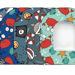 May include: Set of five colorful toilet seat covers with different nautical themed designs. Each cover features a different pattern with crabs, sharks, anchors, and stars.