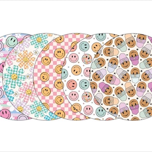 May include: Five round, colorful coasters with different patterns. The patterns include a blue and white striped pattern with white flowers, a pink and white floral pattern, a pink and white checkered pattern, a blue and white smiley face pattern, and a white pattern with brown and purple smiley faces wearing hats.
