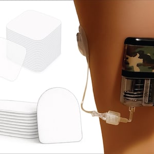 Może przedstawiać: Obraz przedstawia urządzenie medyczne z kamuflażem przymocowane do ramienia osoby. Widoczne są również stosy białych, kwadratowych i owalnych plastrów samoprzylepnych. Urządzenie posiada przezroczysty element z elementami wewnętrznymi.