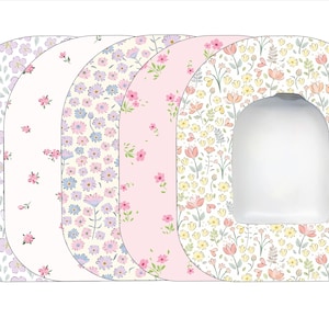 May include: Set of five toilet seat covers with floral patterns. The covers are in shades of pink, purple, and white. Each cover features a different floral design.