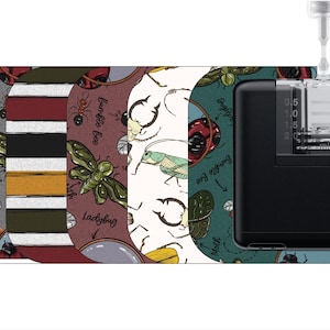 May include: A black and gray electronic device with a clear glass top and a scale on the side. The device is surrounded by five different patterned stickers featuring insects and the words "Earthworm", "Fire Ant", "Moth", "Bumble Bee", "Ladybug", and "Ant".