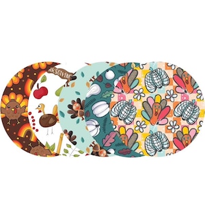 May include: Set of four round Thanksgiving themed paper plates. The plates feature different patterns with turkeys, pumpkins, and fall leaves in shades of orange, brown, green, and white. The text "Thanksgiving" is printed on one of the plates.