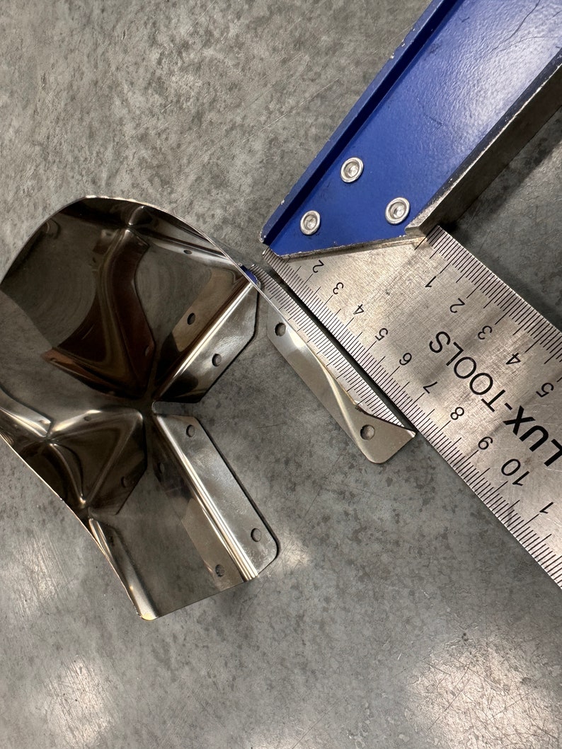 May include: A stainless steel corner bracket with a rounded edge, measured with a blue and silver ruler marked "LUX-TOOLS".