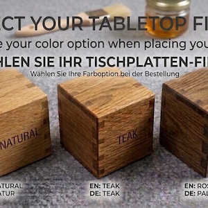 May include: Three wooden cubes labelled "Natural", "Teak", and "Rosewood" are displayed, showcasing tabletop finish options. The image includes text in English and German, guiding the selection of colour options for an order.