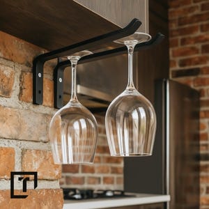Può includere: Portabicchieri in metallo nero fissato a un muro di mattoni, con due bicchieri da vino trasparenti. Il portabicchieri è fissato a una mensola di legno. I bicchieri sono sospesi a testa in giù. Lo sfondo include un ambiente cucina.
