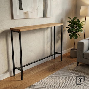 Peut inclure: Une console rectangulaire en bois clair avec un cadre en métal noir. La table est longue et étroite, adaptée pour être placée contre un mur. Le cadre a un design simple et moderne. La table est dans une pièce avec une palette de couleurs neutres.