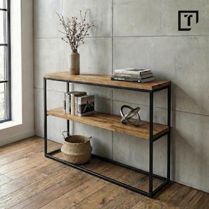 Peut inclure: Console en bois avec une structure en métal noir. La table comporte deux étagères et est décorée de livres, d'une sculpture métallique, d'un panier tressé et d'un vase avec des branches.