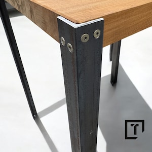 Könnte beinhalten: Nahaufnahme eines Holztisches mit Metallbeinen. Die Beine sind mit Schrauben an der Tischplatte befestigt. Das Metall hat eine rustikale, gealterte Optik.