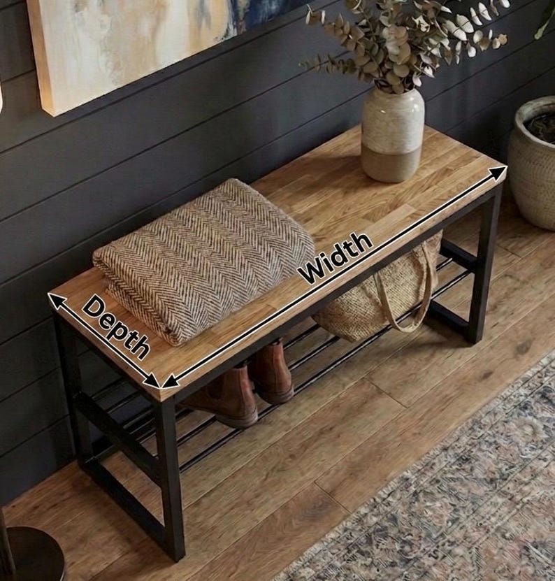 May include: A wooden bench with a black metal frame. The bench has a light brown top and a lower shelf. A folded brown and beige blanket rests on the bench. The bench is 122 cm wide and 41 cm deep.