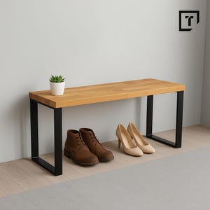 Op de afbeelding: Een houten bank met een lichtbruin blad en zwarte metalen poten. Bruine leren laarzen en beige hoge hakken staan onder de bank. Een kleine plant in een pot staat op het oppervlak van de bank. De bank is voor binnenshuis.