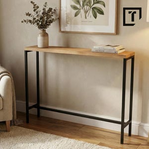 Könnte beinhalten: Ein schmaler Konsolentisch mit einer hellen Holzplatte und schwarzen Metallbeinen. Eine Vase mit getrockneten Zweigen und zwei Büchern steht auf dem Tisch. Ein gerahmter botanischer Druck hängt an der Wand.