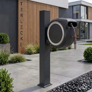 Könnte beinhalten: Eine dunkelgraue Gartenschlauchrolle, die an einem passenden Pfosten befestigt ist. Die Rolle hat ein kreisförmiges Design mit weißem Rand und schwarzem Zentrum. Der Schlauch erstreckt sich nach unten, und der Pfosten ist auf einer Betonoberfläche installiert. Das Wort "TERLECKI" ist vertikal links aufgedruckt.