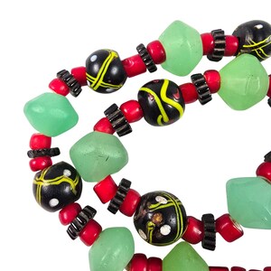 May include: Close-up of a necklace featuring a mix of beads. The necklace has black and yellow patterned beads, red cylindrical beads, light green geometric beads, and black spacers. The beads are strung together, creating a unique jewelry piece.