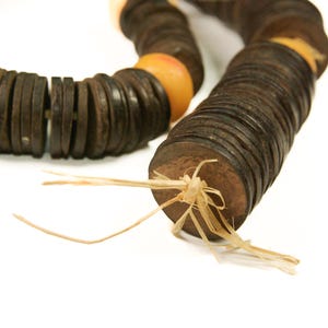 May include: A necklace made of dark brown, round wooden beads and interspersed with orange beads. The necklace is strung on a natural fiber cord, with the ends tied together. The beads are stacked in a spiral pattern.