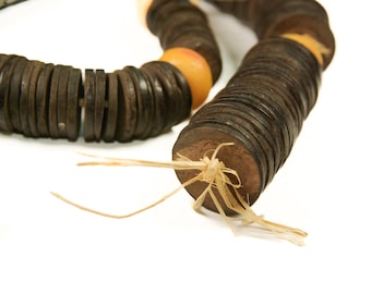 May include: A necklace made of dark brown, round wooden beads and interspersed with orange beads. The necklace is strung on a natural fiber cord, with the ends tied together. The beads are stacked in a spiral pattern.