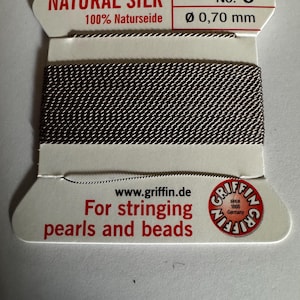 May include: A spool of natural silk thread for stringing pearls and beads. The spool is labeled "NATURAL SILK 100% Naturseide No. 6 Ø 0,70 mm" and "www.griffin.de For stringing pearls and beads GRIFFIN since 1866 Germany".
