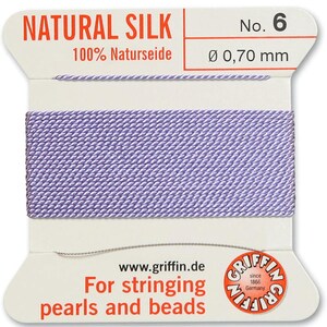 May include: A spool of purple natural silk thread for stringing pearls and beads. The label reads "NATURAL SILK 100% Naturseide No. 6 Ø 0,70 mm" and "For stringing pearls and beads".