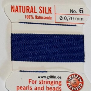 May include: A spool of dark blue natural silk thread for stringing pearls and beads. The spool is labeled "NATURAL SILK 100% Naturseide No. 6 Ø 0,70 mm" and "www.griffin.de For stringing pearls and beads".