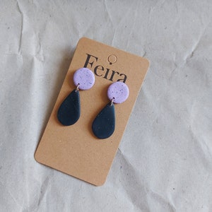 May include: A pair of dangle earrings with a purple and black speckled design. The earrings are on a brown card with the word "Feira" printed on it.