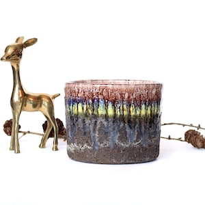 Könnte beinhalten: Ein brauner Keramiktopf mit blauer, gelber und weißer Glasur. Der Topf hat eine raue, strukturierte Oberfläche und eine breite, runde Öffnung.