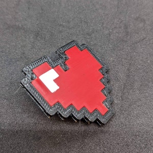 May include: A red pixelated heart shape with a white outline, printed in 3D with a black border.
