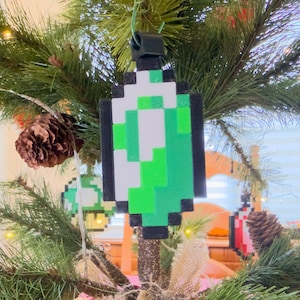 May include: A decorated Christmas tree with pixelated ornaments in various colors, including blue, green, and red. The ornaments are shaped like gems and hearts. Pine cones and string lights add to the festive holiday decor.