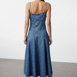K&ouml;nnte beinhalten: Ein blaues Jeans-Midikleid mit einem figurbetonten Oberteil und einem ausgestellten Rock. Das Kleid hat einen Rei&szlig;verschluss auf der R&uuml;ckseite und einen runden Ausschnitt.
