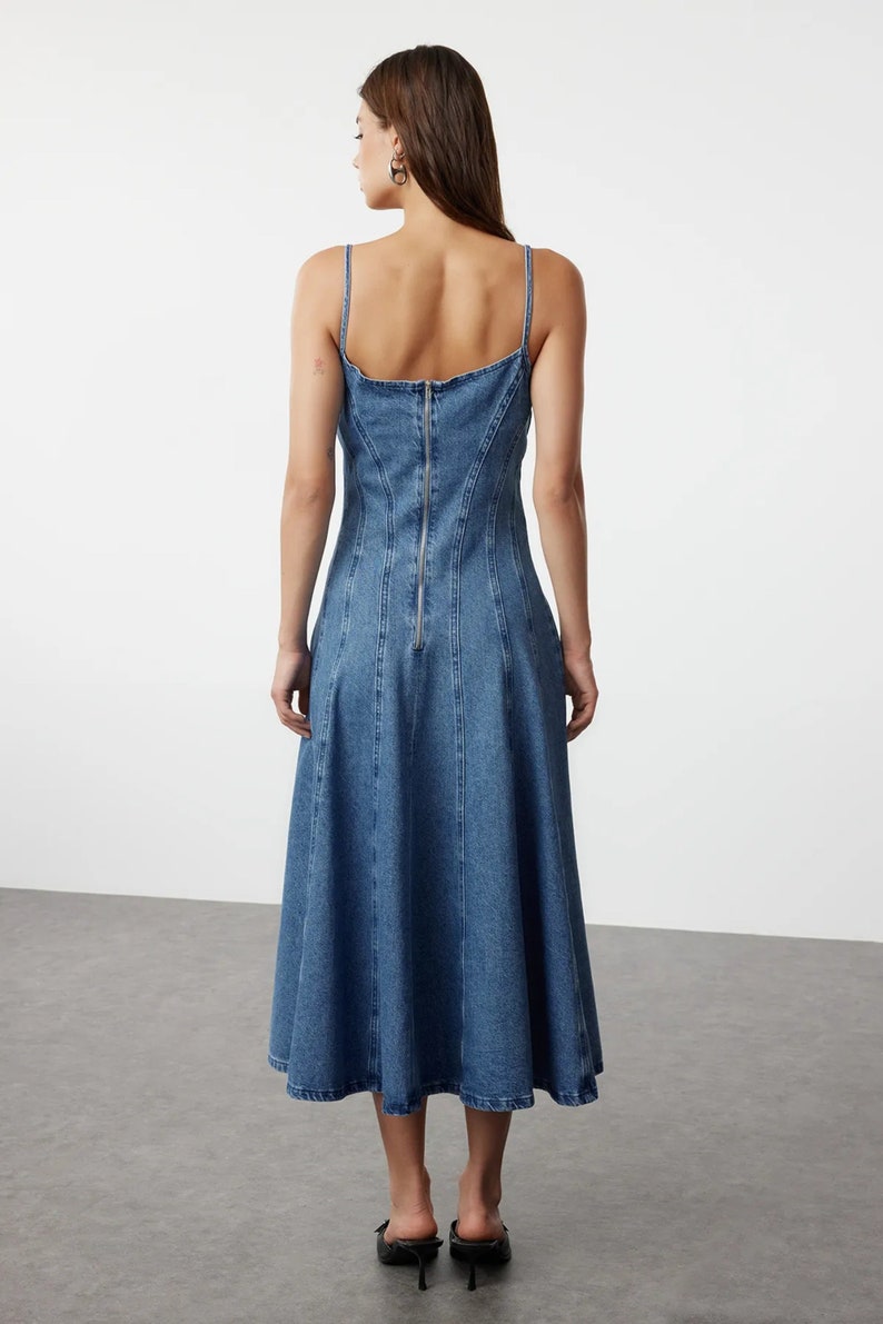 K&ouml;nnte beinhalten: Ein blaues Jeans-Midikleid mit einem figurbetonten Oberteil und einem ausgestellten Rock. Das Kleid hat einen Rei&szlig;verschluss auf der R&uuml;ckseite und einen runden Ausschnitt.