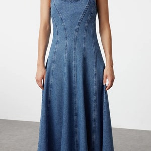 K&ouml;nnte beinhalten: Ein blaues Jeans-Midikleid mit einem figurbetonten Oberteil und einem ausgestellten Rock. Das Kleid hat d&uuml;nne Tr&auml;ger und einen runden Ausschnitt.