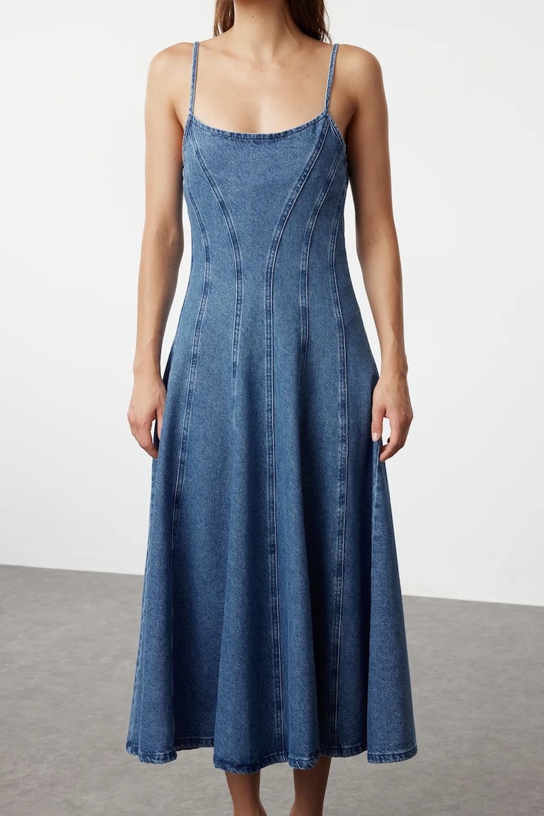 K&ouml;nnte beinhalten: Ein blaues Jeans-Midikleid mit einem figurbetonten Oberteil und einem ausgestellten Rock. Das Kleid hat d&uuml;nne Tr&auml;ger und einen runden Ausschnitt.