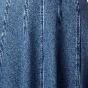 K&ouml;nnte beinhalten: Nahaufnahme einer blauen Jeansrock mit ausgestelltem Saum und mehreren vertikalen N&auml;hten.