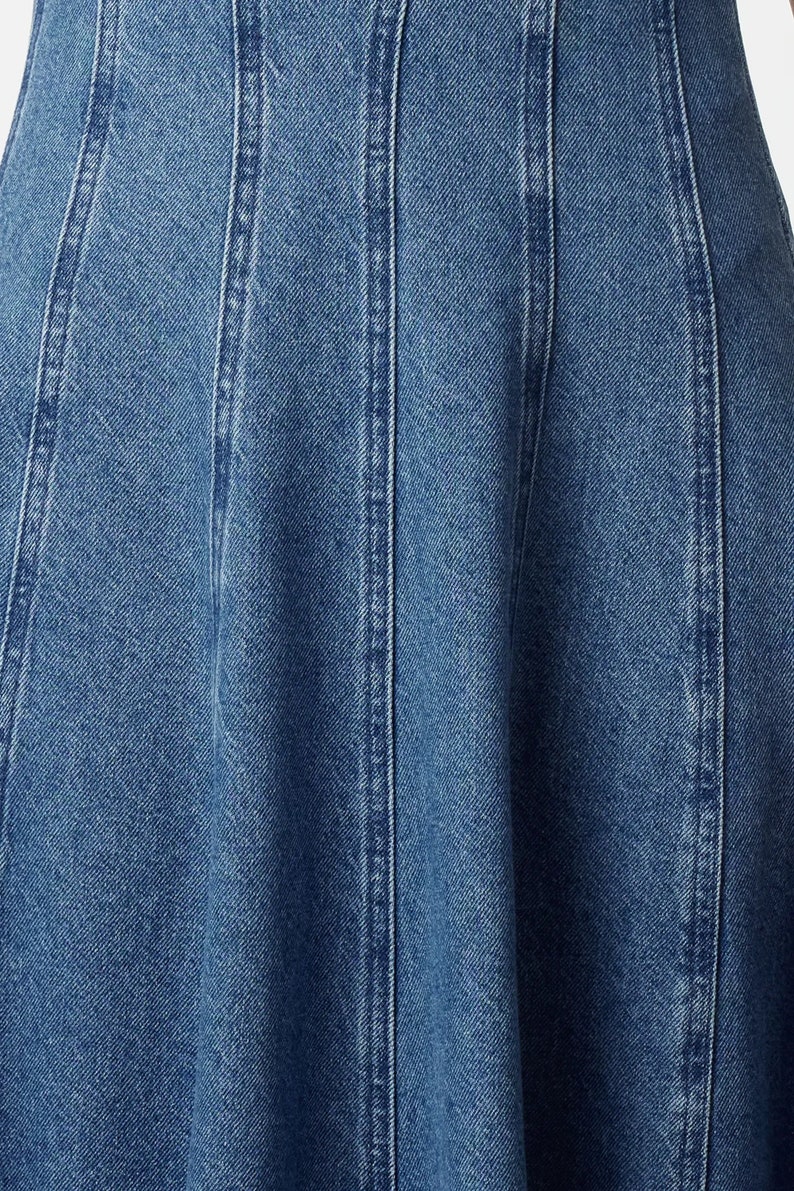 K&ouml;nnte beinhalten: Nahaufnahme einer blauen Jeansrock mit ausgestelltem Saum und mehreren vertikalen N&auml;hten.